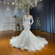 Full-length front view of a model wearing an elegant lace mermaid wedding dress with long sleeves, a beaded illusion neckline, and a voluminous romantic train in a luxury bridal showroom.