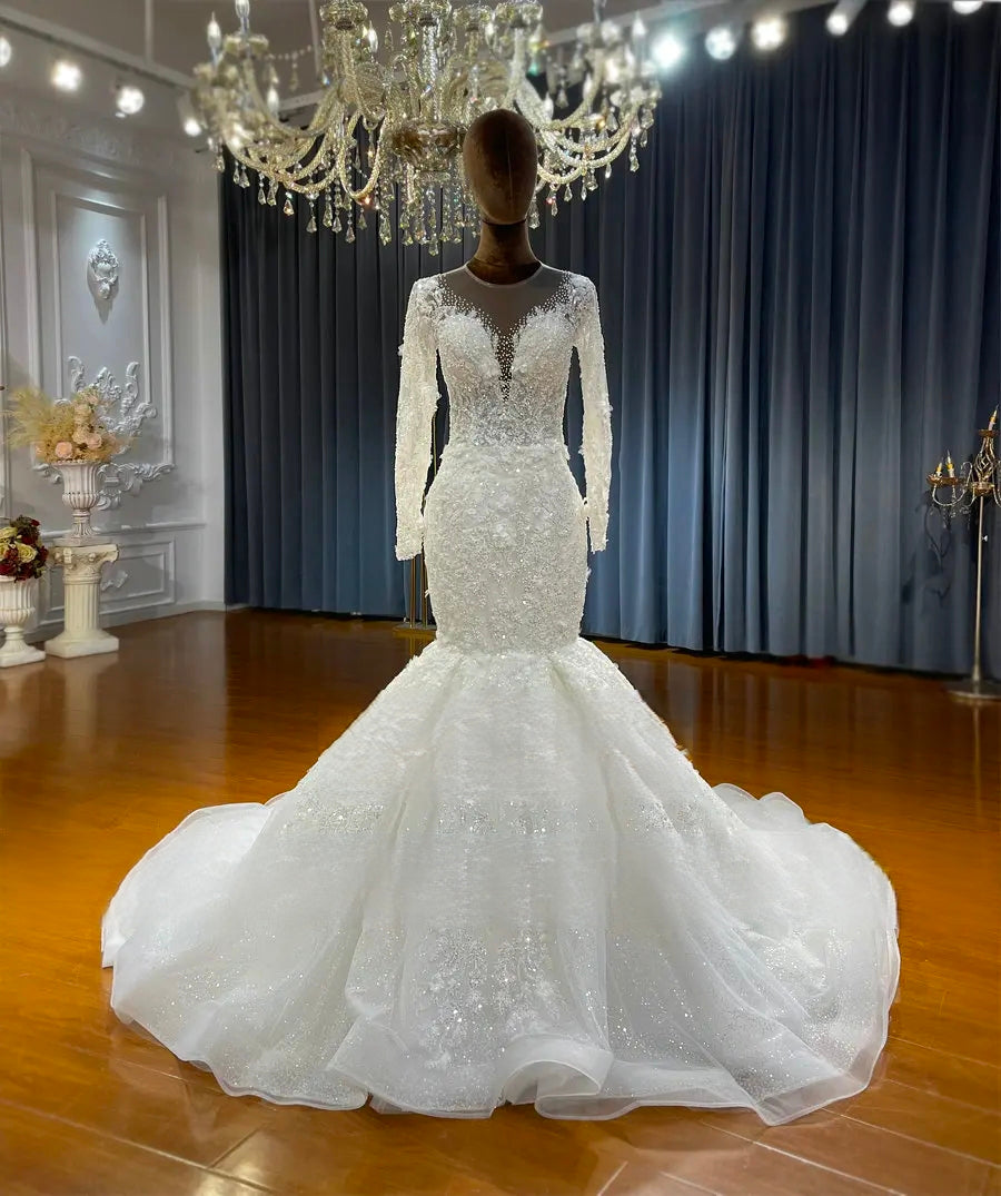 Long sleeve lace mermaid bridal gown on a mannequin, showcasing the heavily embellished bodice, fitted silhouette, and flared glitter tulle skirt.