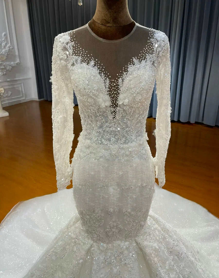 Close-up detail of a wedding dress bodice featuring delicate illusion mesh, pearl beading along the V-neckline, and intricate floral lace appliques.