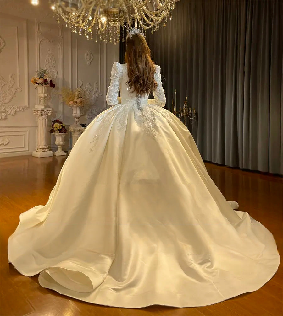 Rear view of a modest long-sleeved bridal gown featuring an expansive white satin cathedral train and delicate lace embroidery on the bodice.