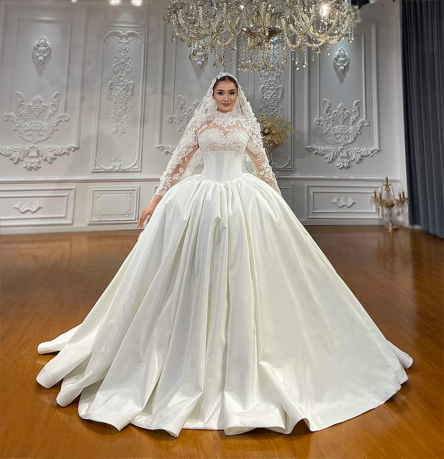 Front-facing view of a luxury nude taffeta bridal dress with a pleated ball gown skirt and long-sleeve lace detailing.