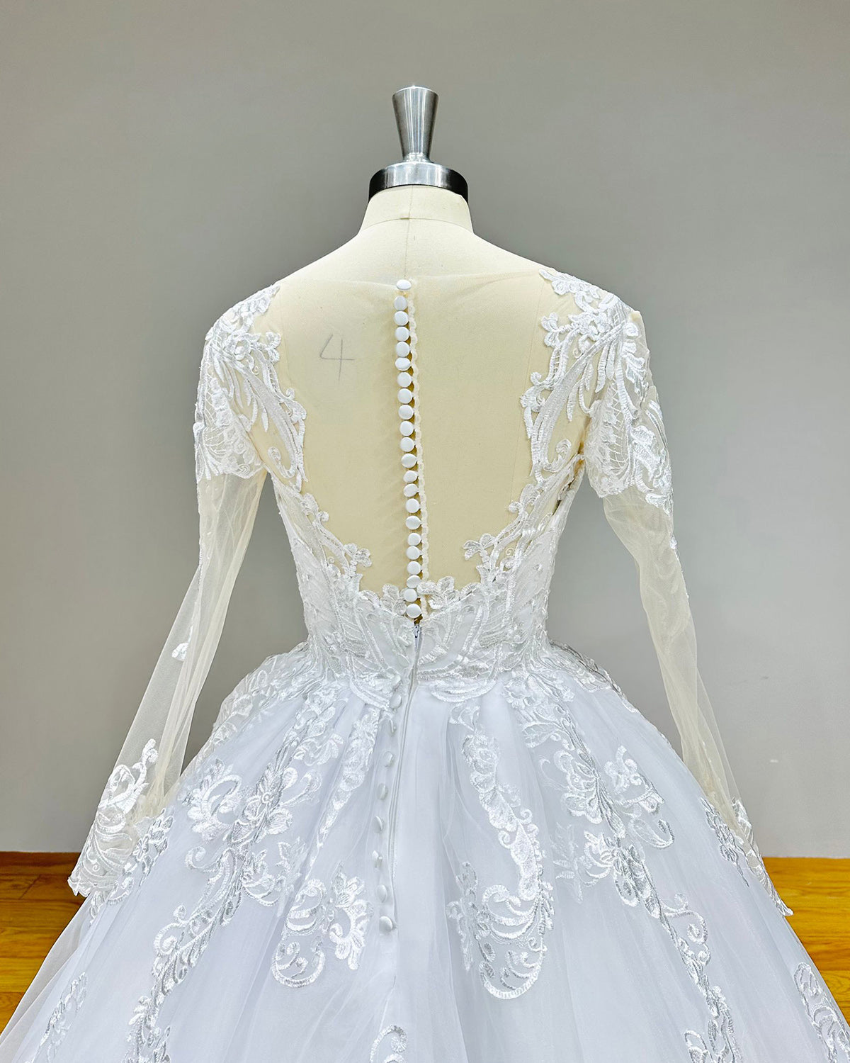 Close-up back bodice detail of an elegant wedding dress, featuring a stunning illusion back, delicate button closures, and fine lace details.