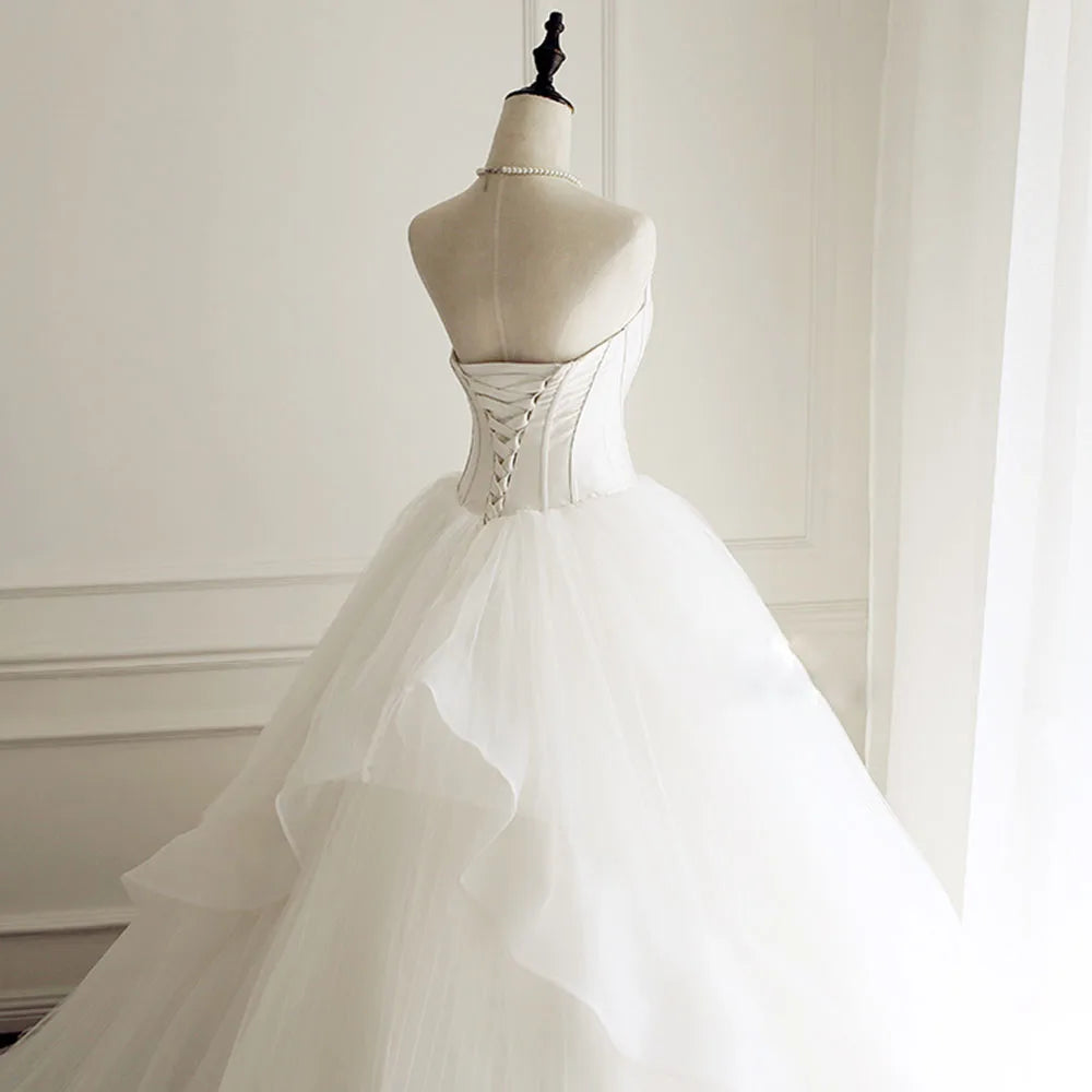 Back view of a sleeveless A-line wedding dress on a mannequin, highlighting the intricate lace-up corset back and tiered train.