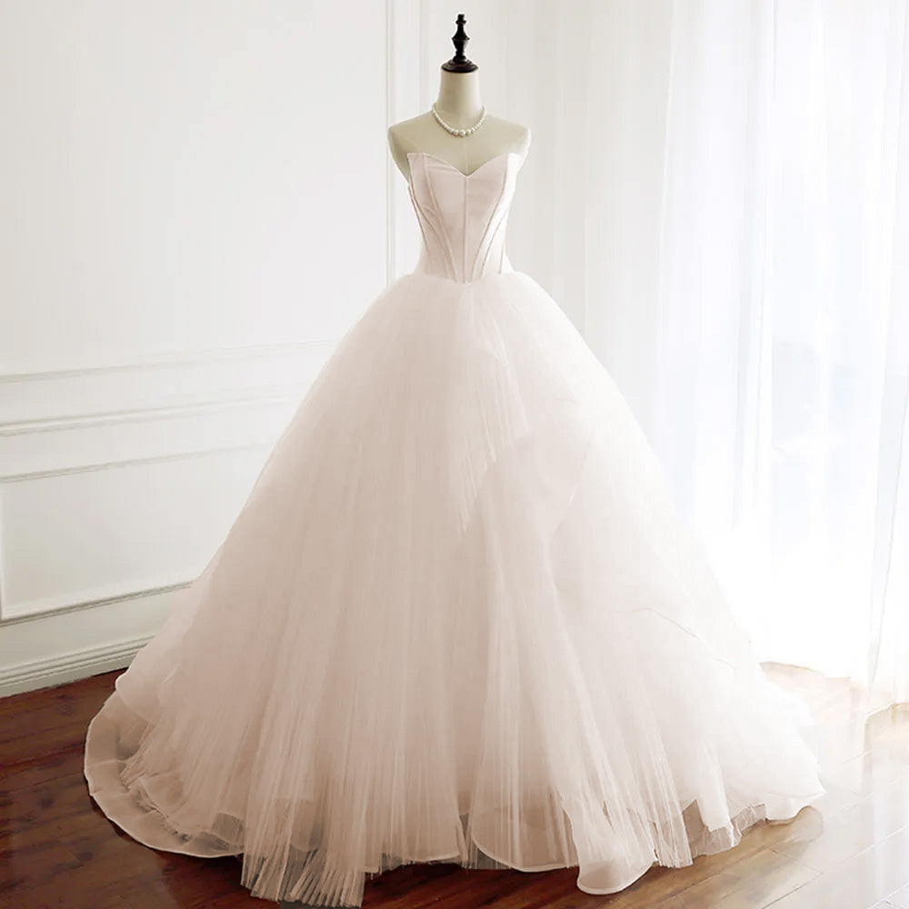 A pink-toned strapless A-line wedding dress on a mannequin, showcasing a structured bodice and voluminous layered tulle skirt.