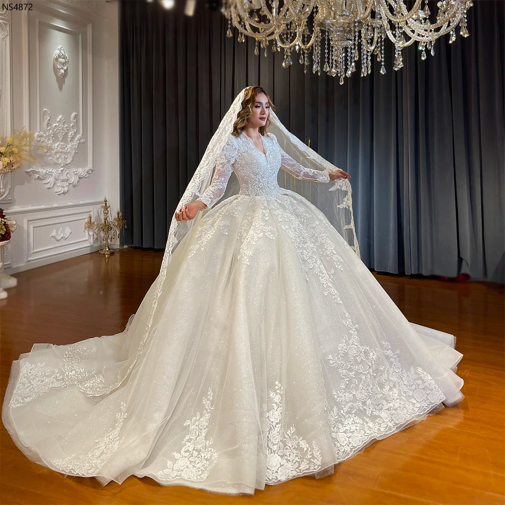 Full-length side perspective of a luxury off-white long sleeve wedding dress with a dramatic shimmering cathedral train spread wide across a polished floor.