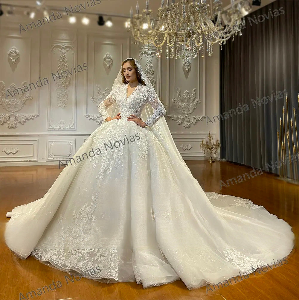 Front-facing bridal portrait of a model showcasing the intricate lace bodice, V-neckline, and expansive sparkling skirt of a luxury off-white ball gown wedding dress.