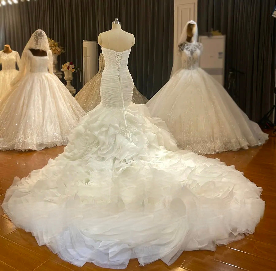 Rear view of the mermaid wedding gown on a mannequin, highlighting the elegant lace-up corset back and an expansive layered organza ruffled train.