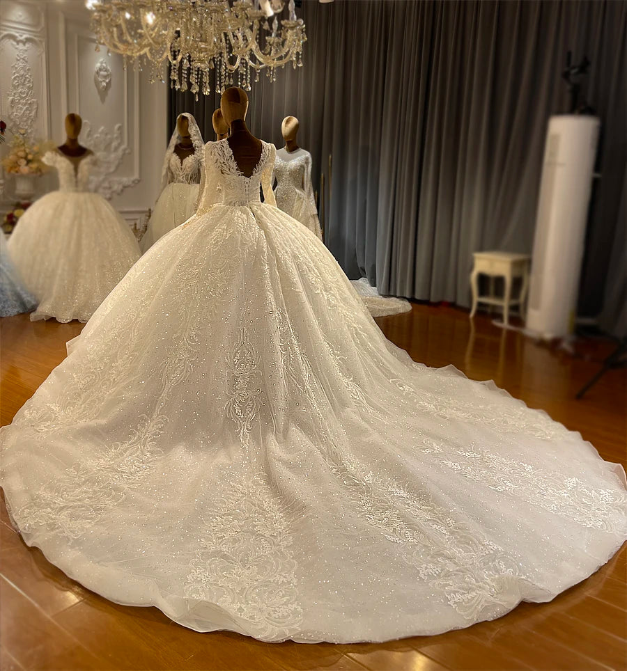 Rear view of a new stylish bridal dress on a mannequin, showcasing a dramatic cathedral-length train with intricate lace appliqués and a V-back.