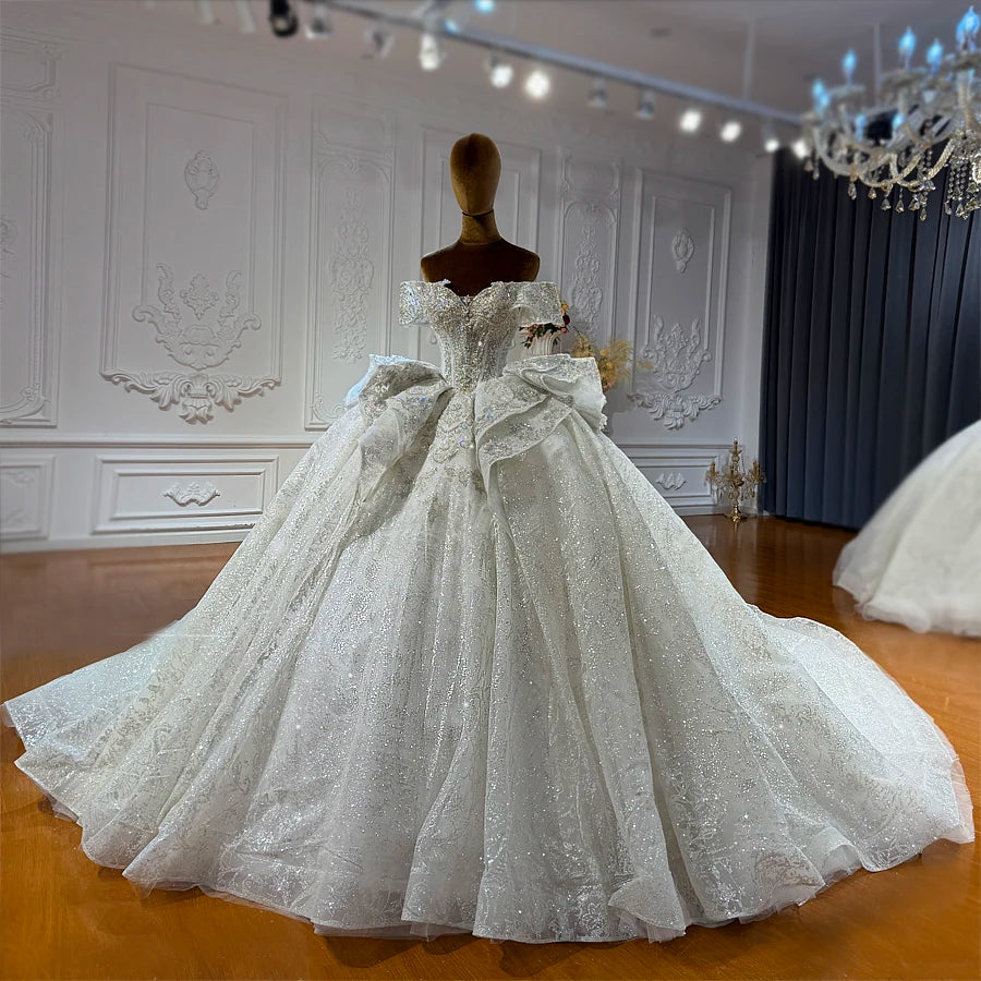Full-length view of an elegant off-the-shoulder bridal gown featuring a voluminous ball gown skirt and shimmering silver sequin embellishments.