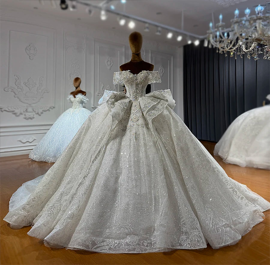 Front-facing shot of a luxury off-the-shoulder ball gown showcasing a full-length flowing skirt with intricate colorful sequin embroidery.