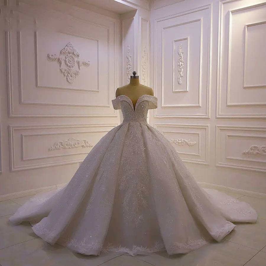 Front view of an elegant full lace wedding gown with off-shoulder sleeves and a structured corset bodice in a studio setting.