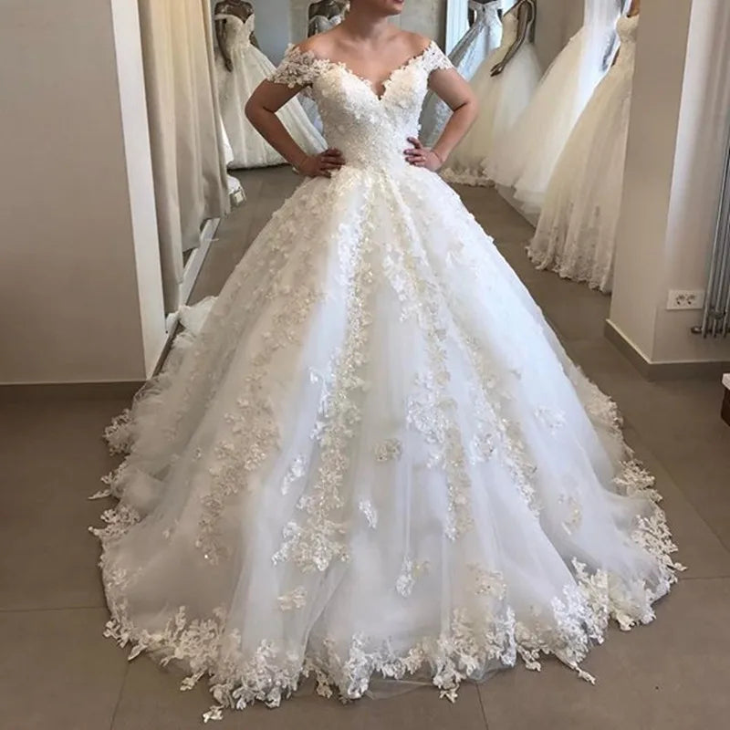 Elegant off-shoulder ball gown wedding dress featuring elaborate floral lace applique and a dramatic voluminous tulle skirt.