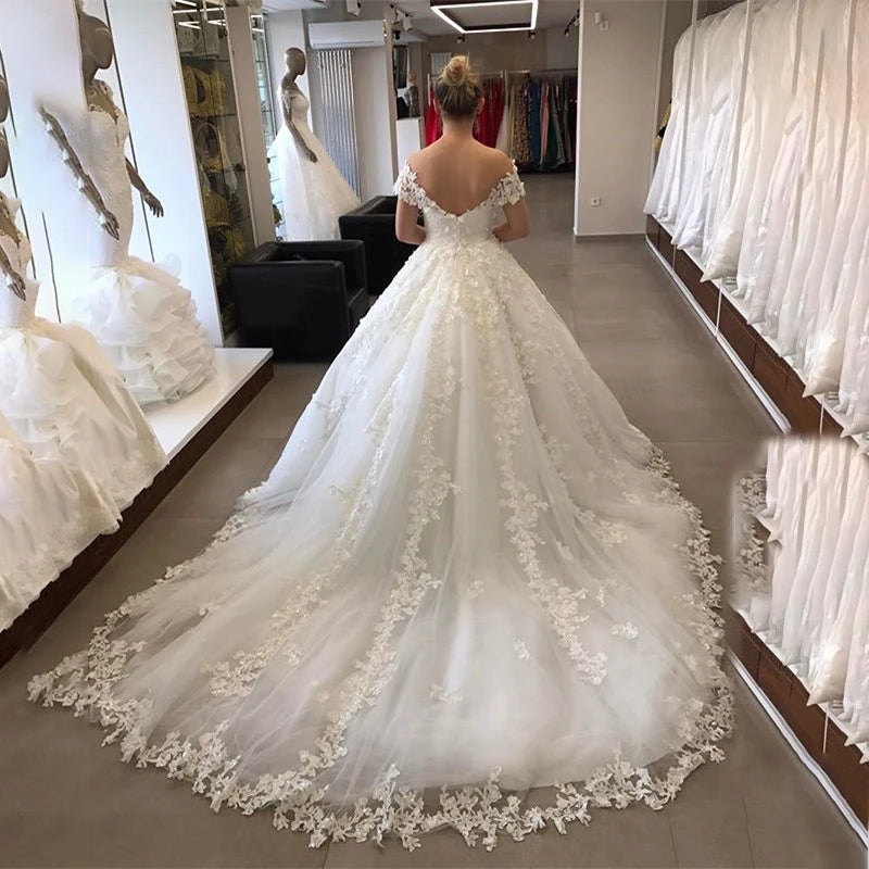 Back view of a luxurious wedding ball gown with a lace-up corset back, off-shoulder neckline, and an extensive chapel train with lace trim.
