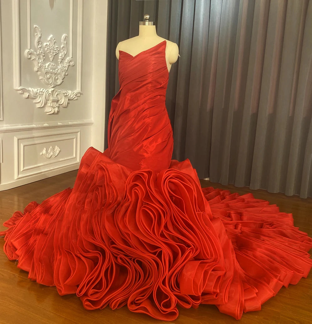 Elegant red satin mermaid wedding dress on a mannequin, showcasing the asymmetrical bodice and a spectacular ruffled skirt with a long train.