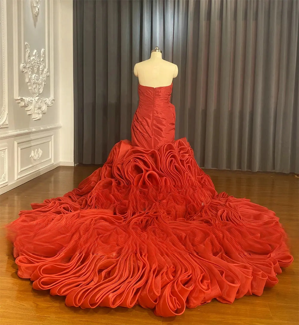 Rear view of the red satin wedding dress on a mannequin, highlighting the dramatic ruffled long train cascading onto a wooden floor.