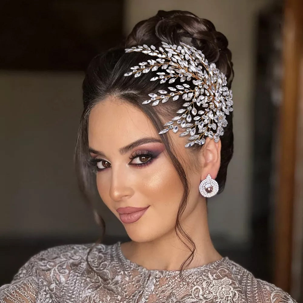 Side profile portrait of a bride showcasing an elegant rhinestone bridal headpiece with a sprawling silver leaf branch design pinned into a high bun updo.