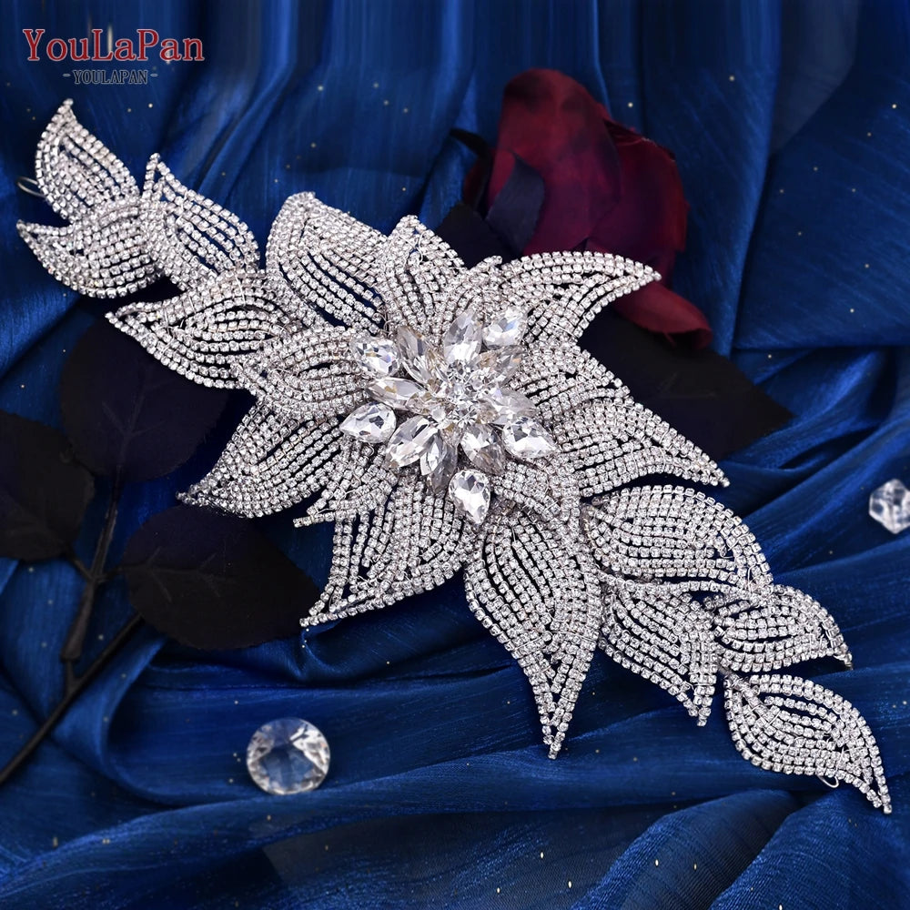 Flat lay view of the YouLaPan premium wedding hair accessory, highlighting a dense, sparkling pave rhinestone flower and leaf layout resting over a blue satin backdrop.