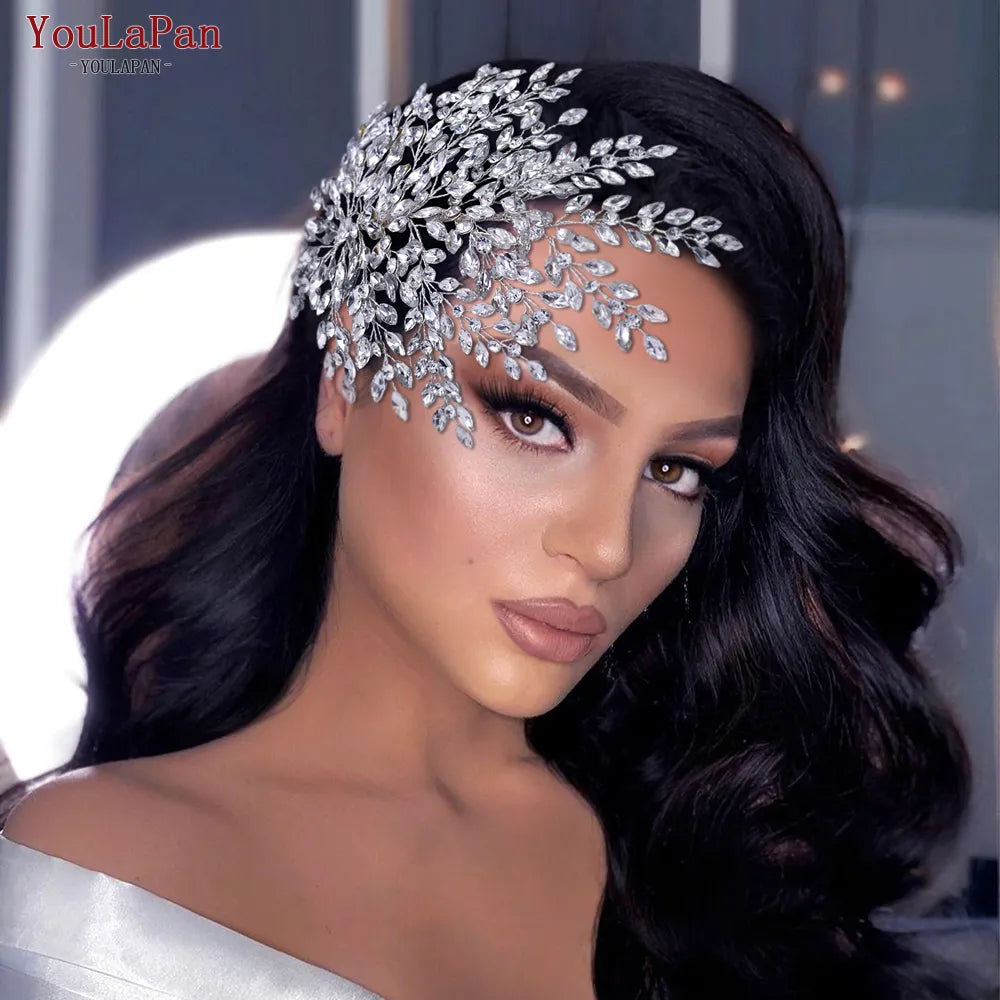 Front portrait of a model with voluminous wavy hair wearing the oversized silver rhinestone bridal headpiece as a dramatic side-swept hair clip statement.