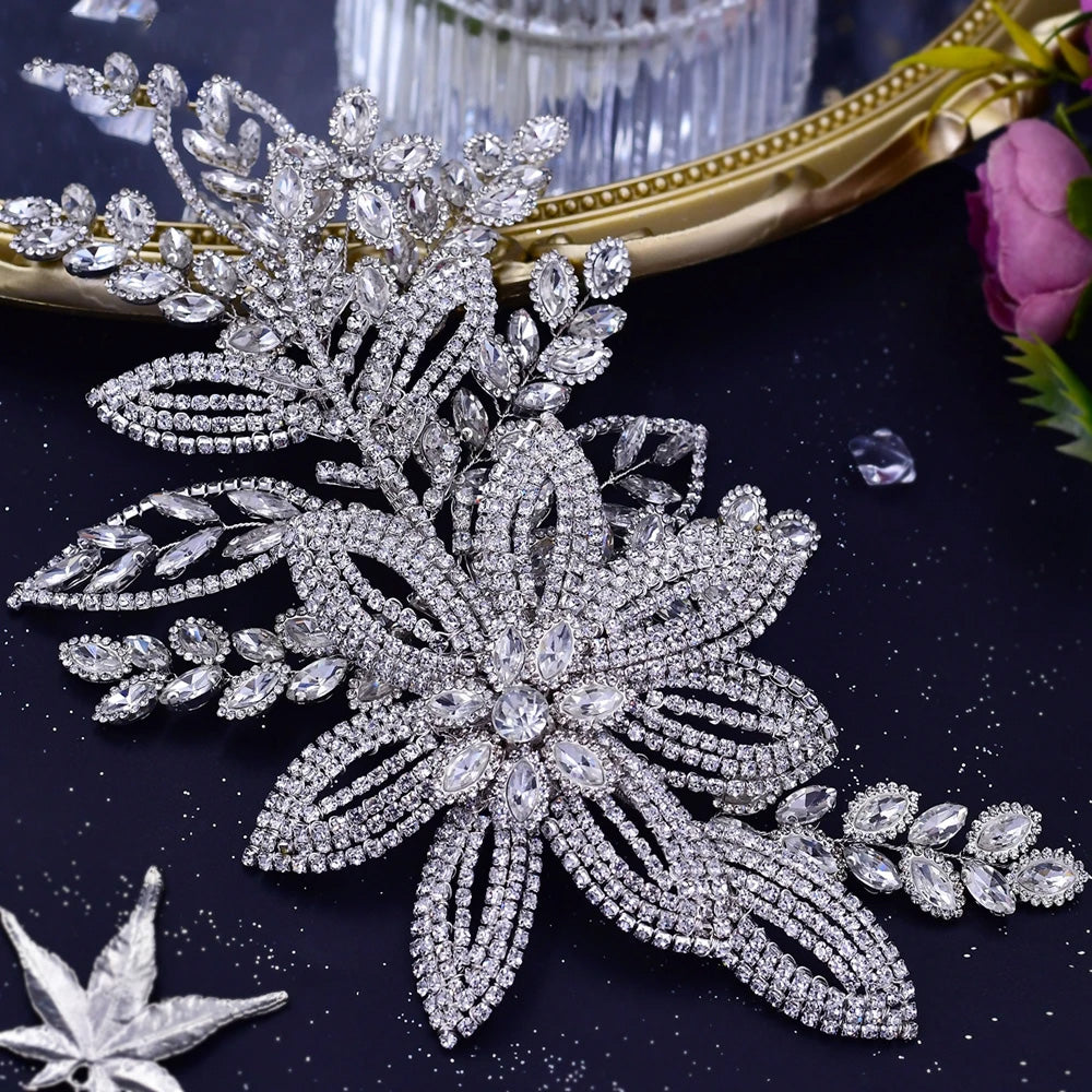 Macro photograph of a sparkling silver bridal headpiece featuring a prominent rhinestone flower motif and outstretched pave crystal leaf branches.