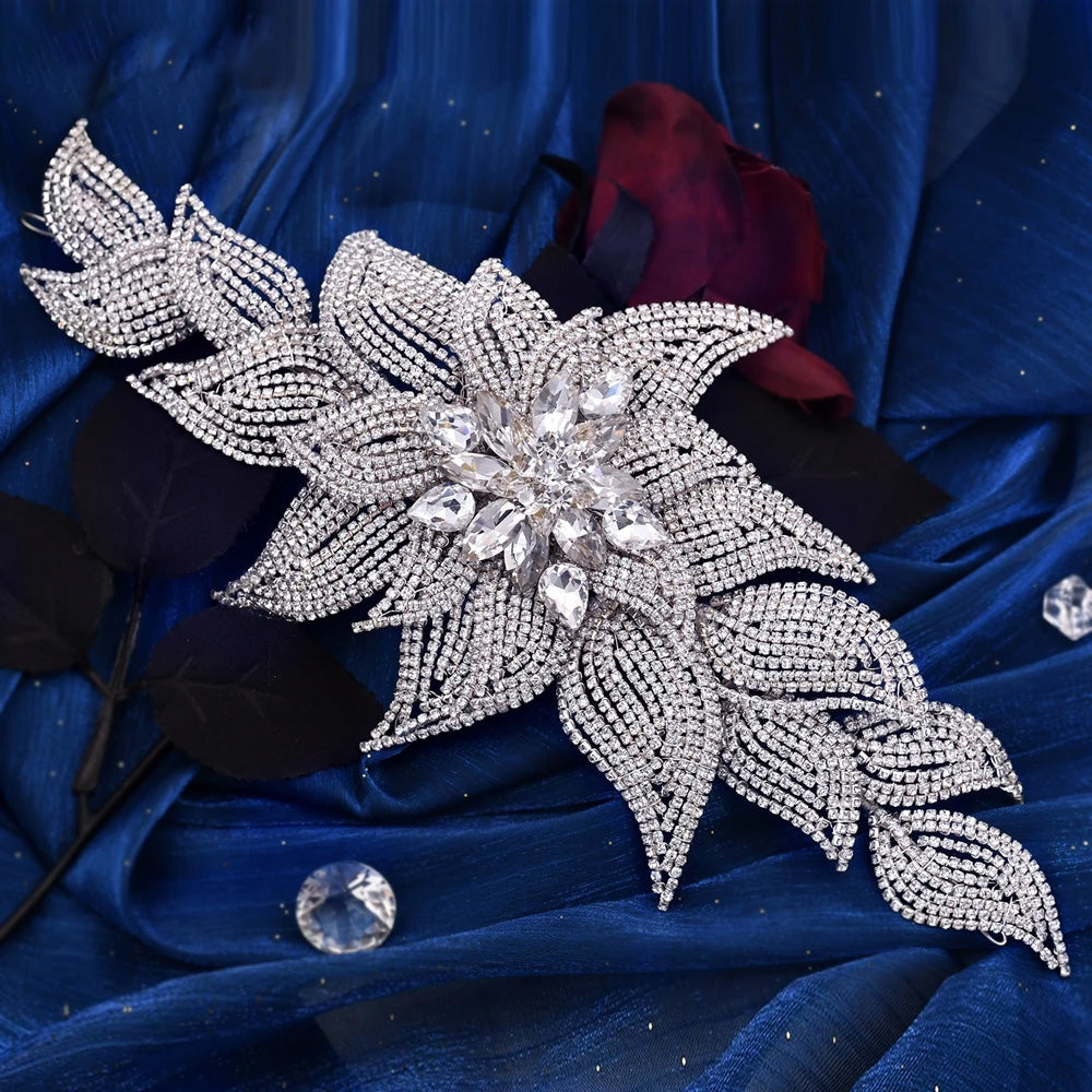 Flat lay overhead view of an elegant rhinestone bridal headpiece featuring a large crystal blossom cluster and pave-set leaf vines on dark blue satin.