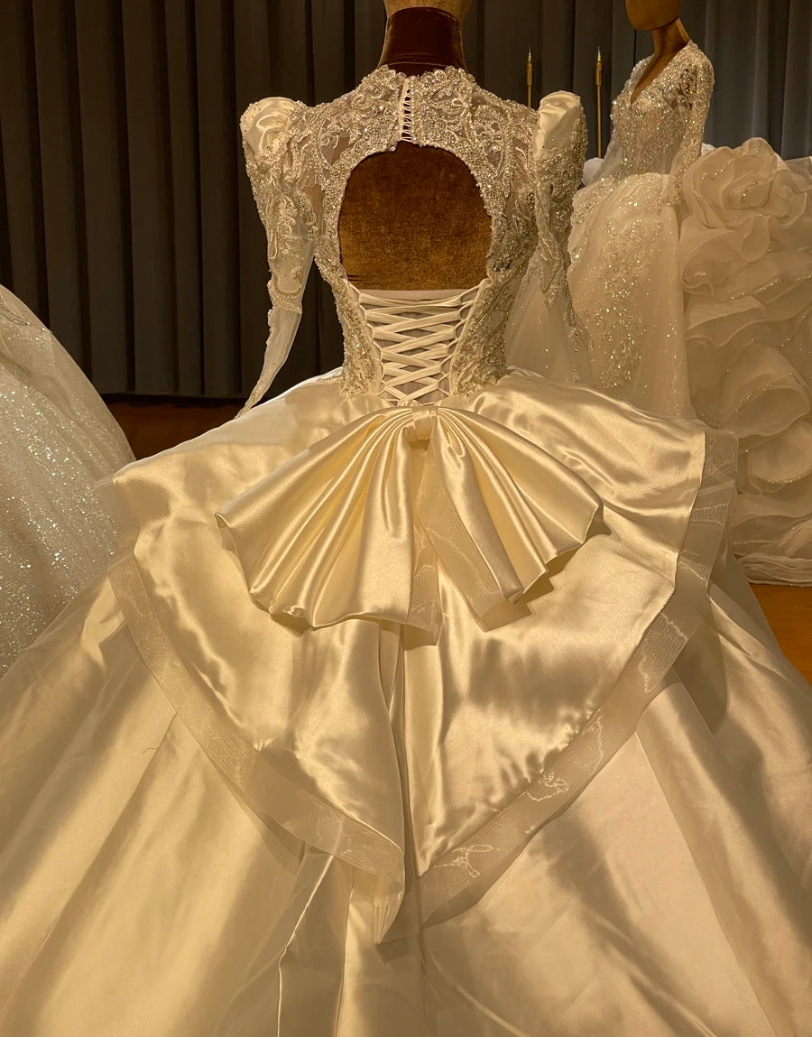 Close-up of a wedding dress back featuring a keyhole lace cut-out, beaded puff sleeves, and a tiered satin peplum waist.