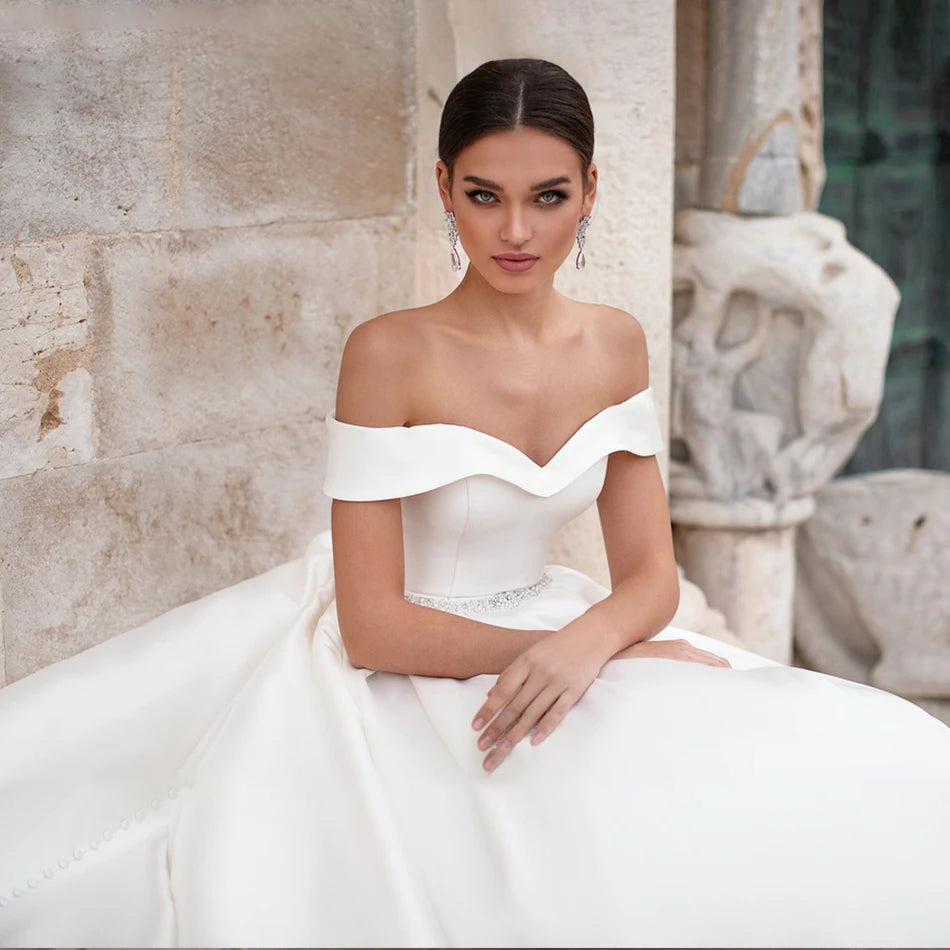 Portrait of a bride in an elegant satin wedding dress, focusing on the refined cap sleeves and detailed crystal sash.