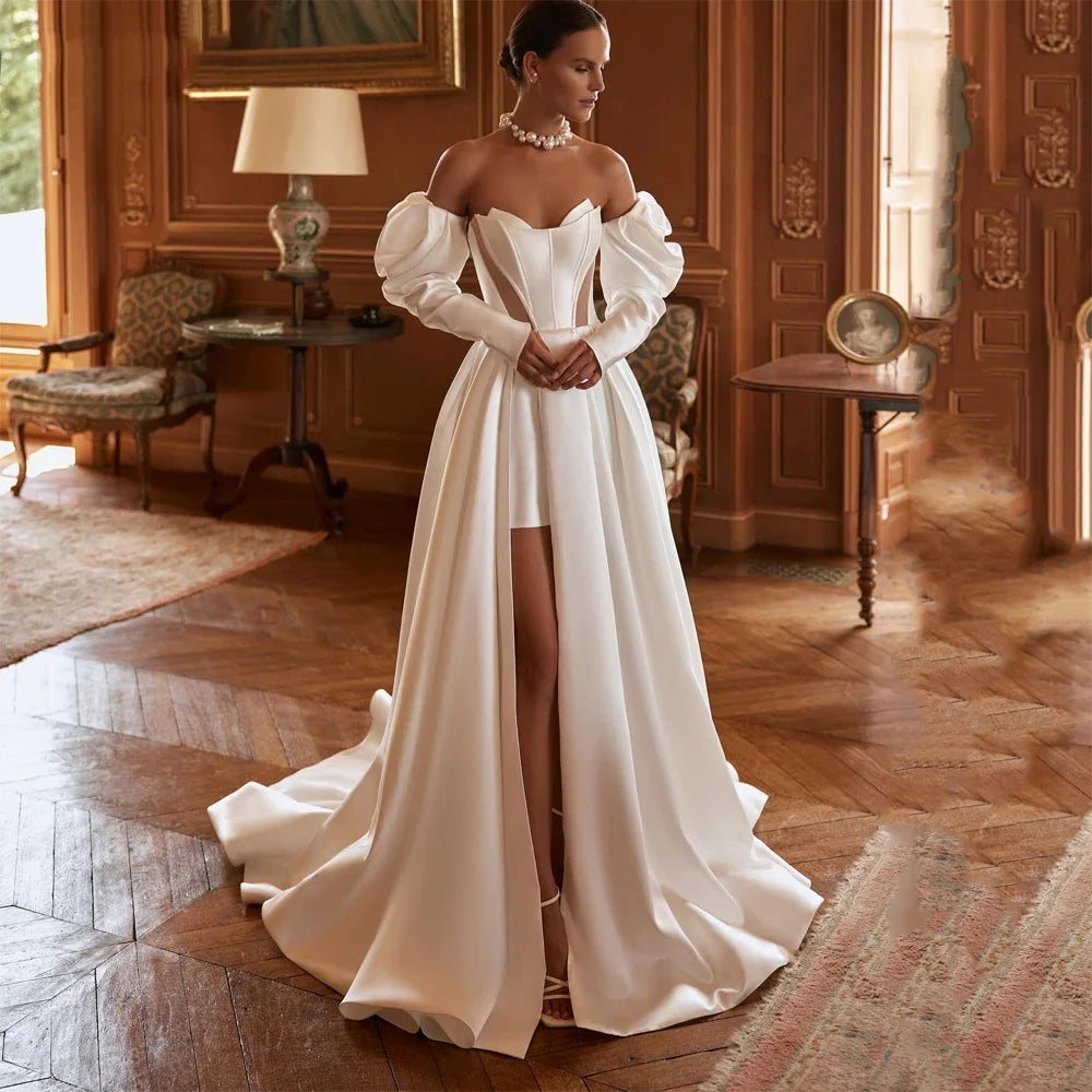 A bride posing in an off-the-shoulder A-line wedding dress with a high-slit skirt, featuring a structured corset bodice and dramatic puff sleeves.