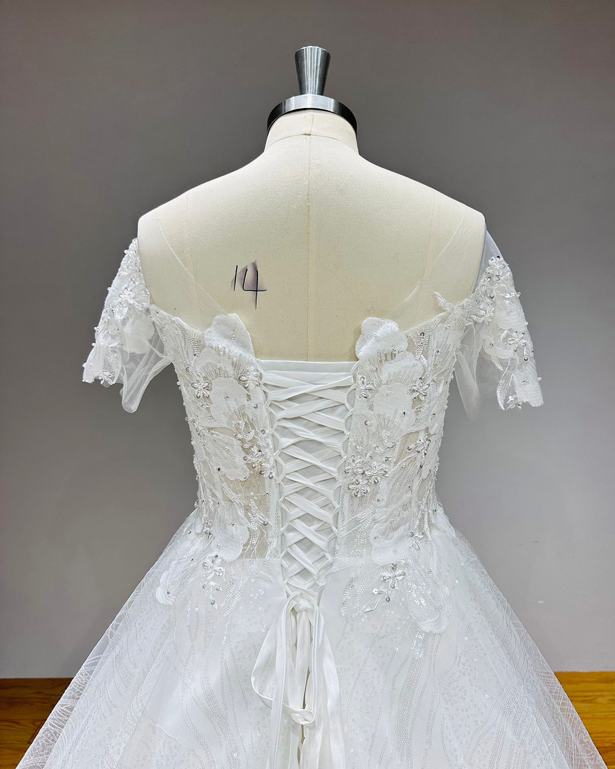Close-up detail of the adjustable satin ribbon tie corset back on an off-the-shoulder sequined wedding dress.