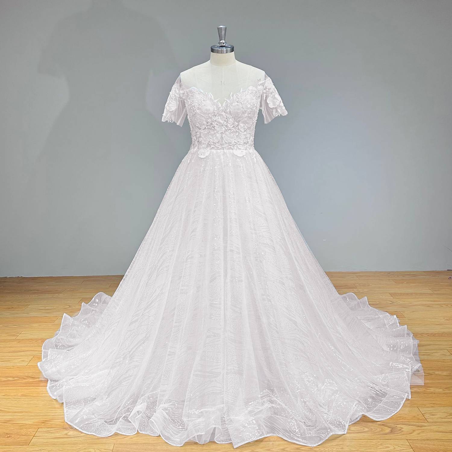 Full-length front view of a sequined white A-line wedding dress with short sleeves and a scalloped hem train on a boutique mannequin.