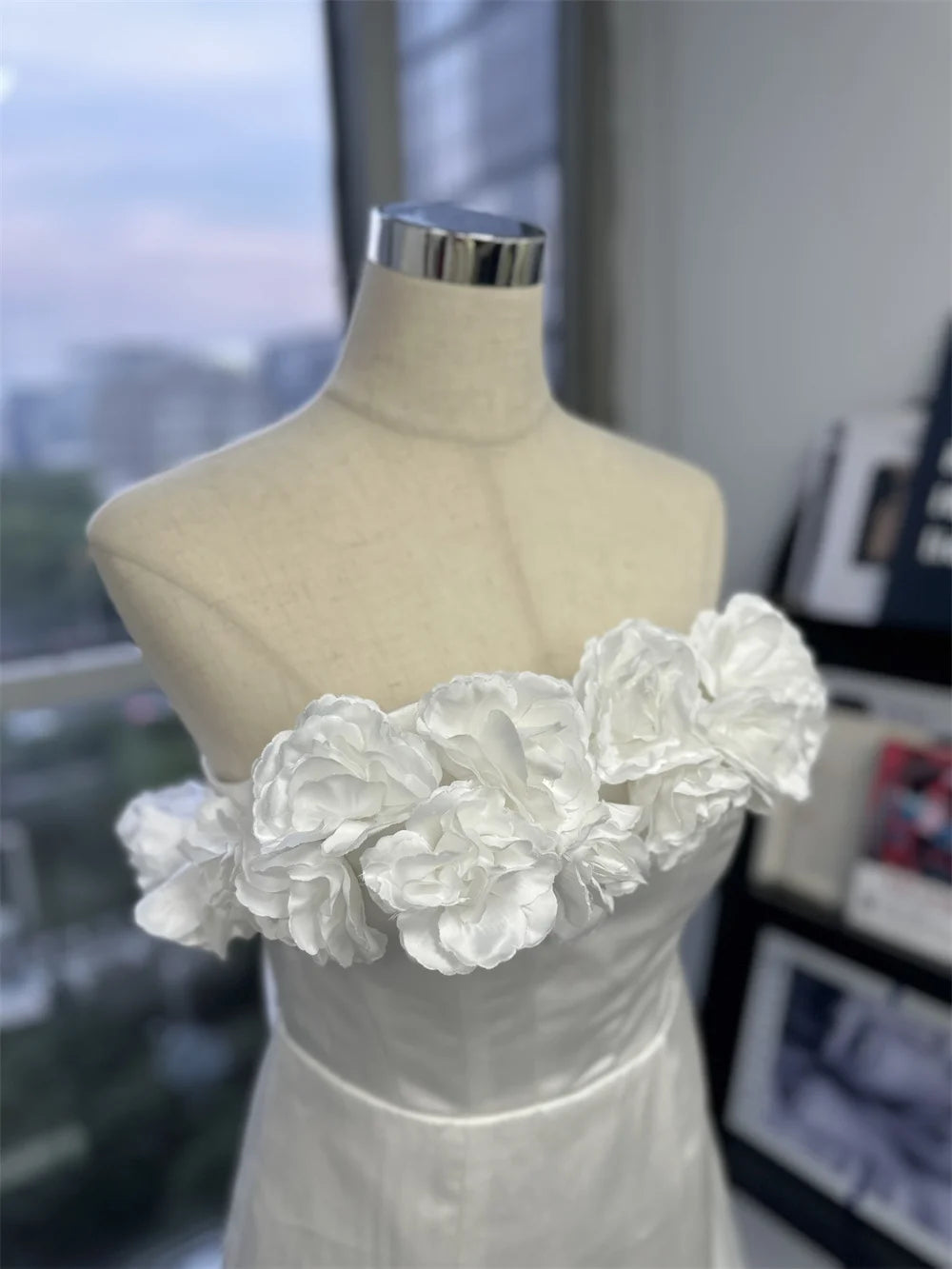 A model standing by a stone pillar wearing a white, off-the-shoulder mini wedding dress with detailed floral appliqués.