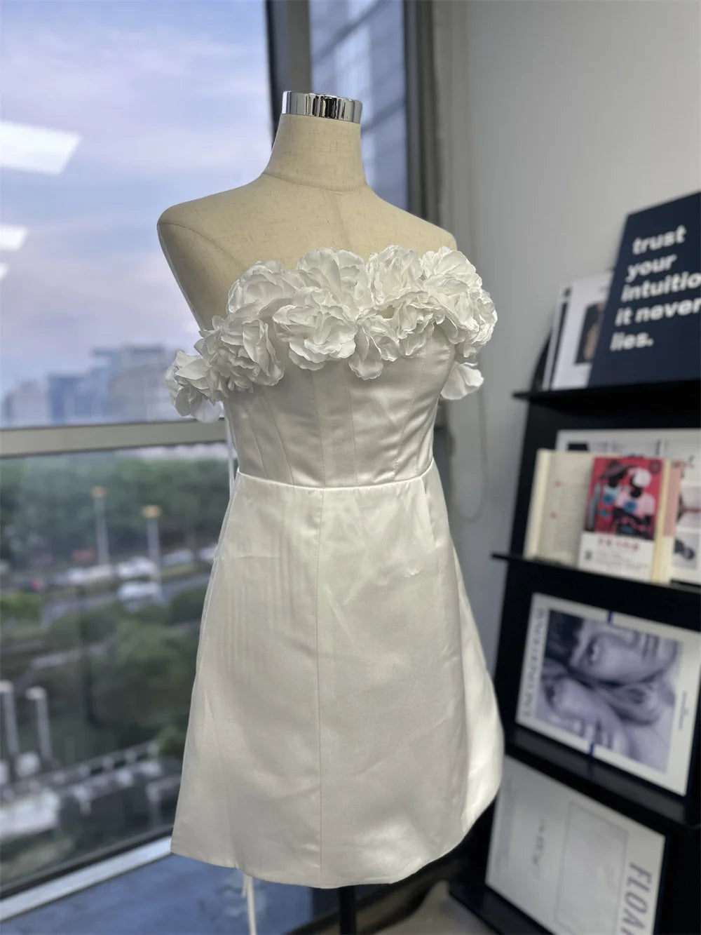 Studio flat lay of a white off-the-shoulder mini wedding dress with 3D floral appliqués and a daring side leg slit.