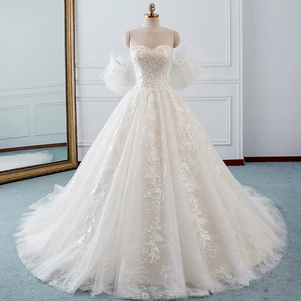 Full-length front profile of an A-line bridal gown with intricate lace appliques and detachable ruffled sleeves on a mannequin.