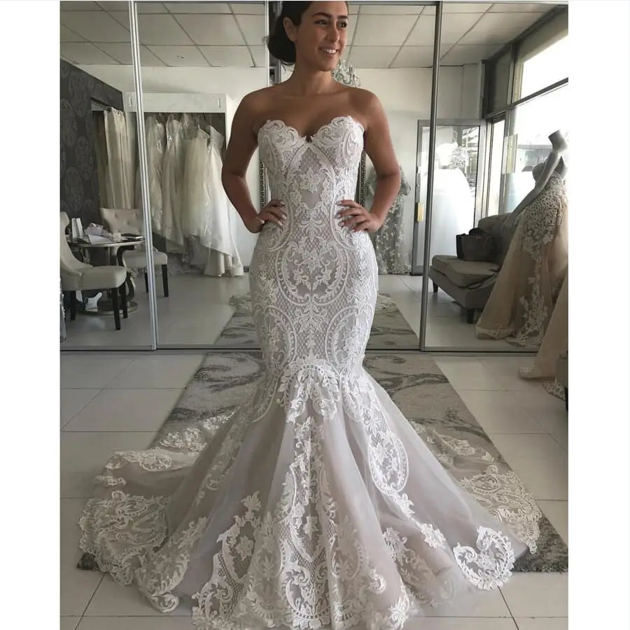 Front view of a model wearing an elegant strapless sweetheart neckline lace mermaid wedding dress with a fitted silhouette and a dramatic flared skirt.