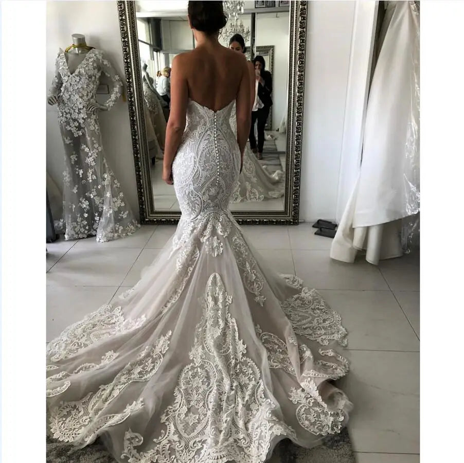 Back view of a lace mermaid wedding gown featuring a low open back with button closures and a romantic, long flowing lace train.
