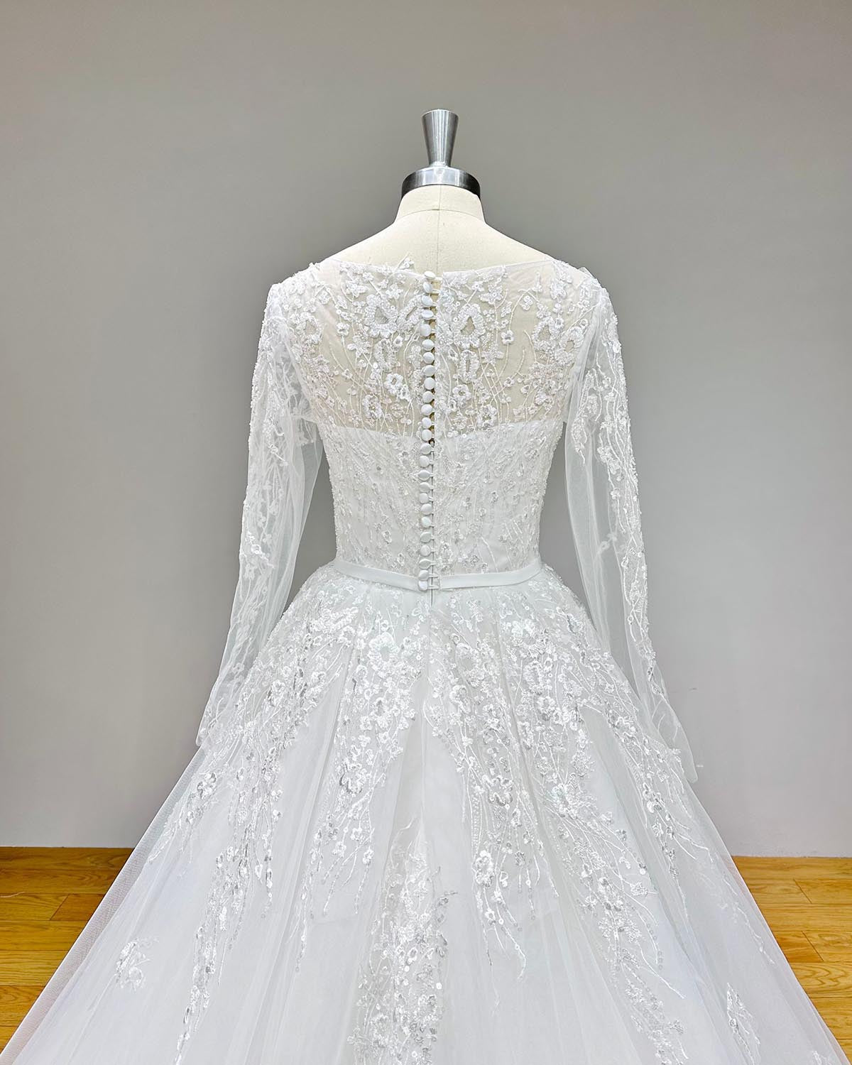 Full back view of an A-line tulle wedding dress with a long train and button-up closure displayed on a mannequin.