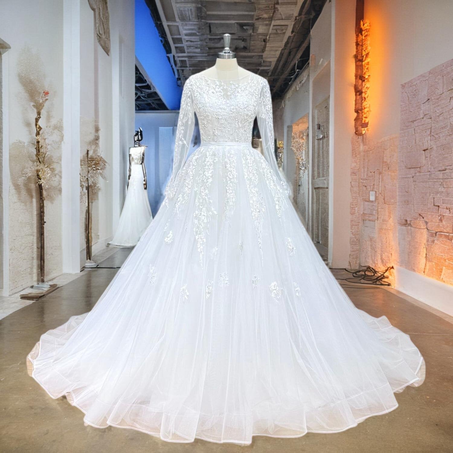 Front view of an elegant long-sleeve A-line tulle wedding dress featuring intricate lace detailing and a satin belt displayed on a mannequin.