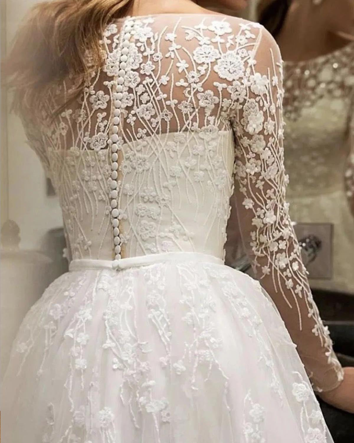 Detailed close-up of the back of a long-sleeve bridal gown showing intricate floral lace, button closure, and sheer illusion fabric.
