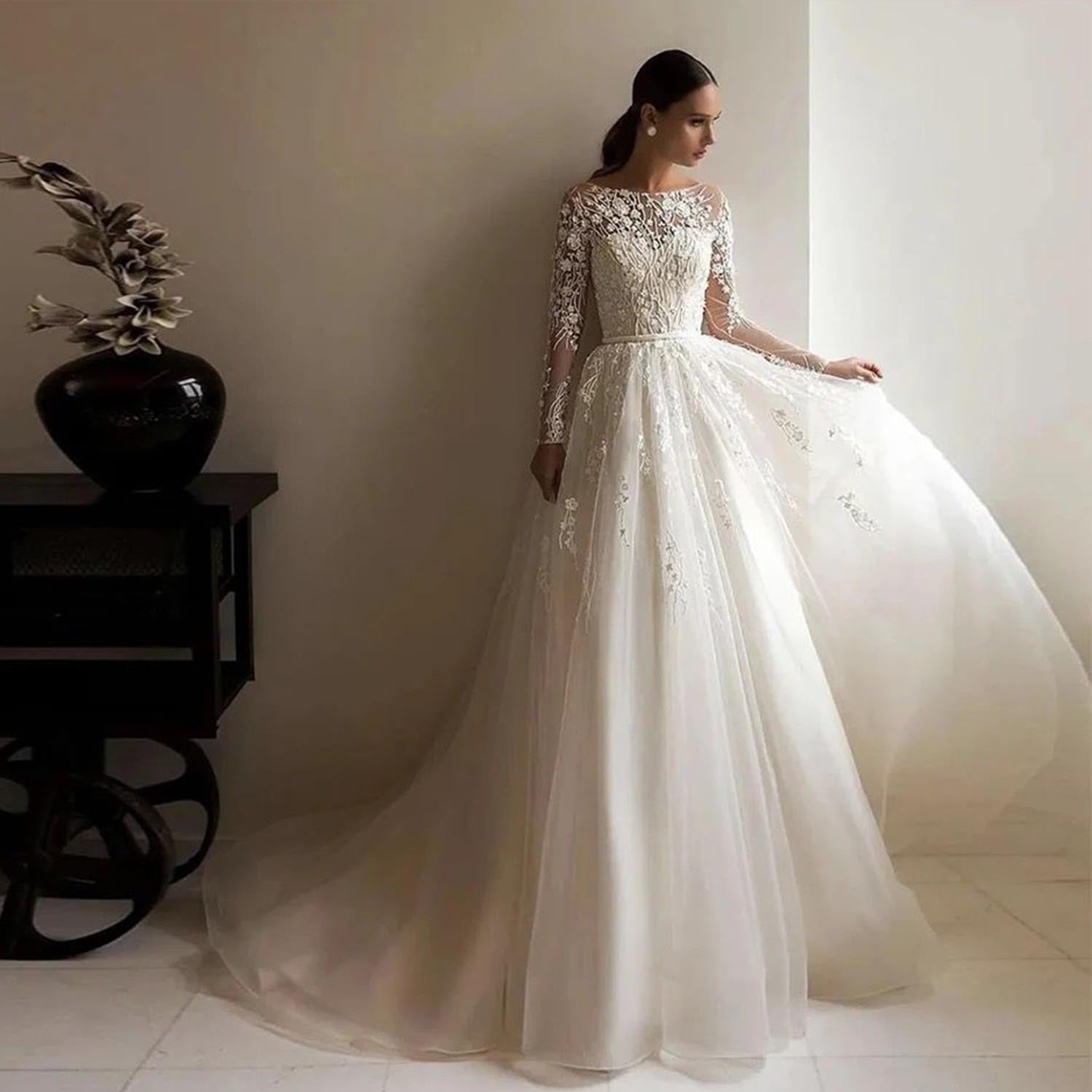 A bride posing in an elegant long-sleeve A-line tulle wedding dress with a satin belt, showing the graceful flow of the skirt.