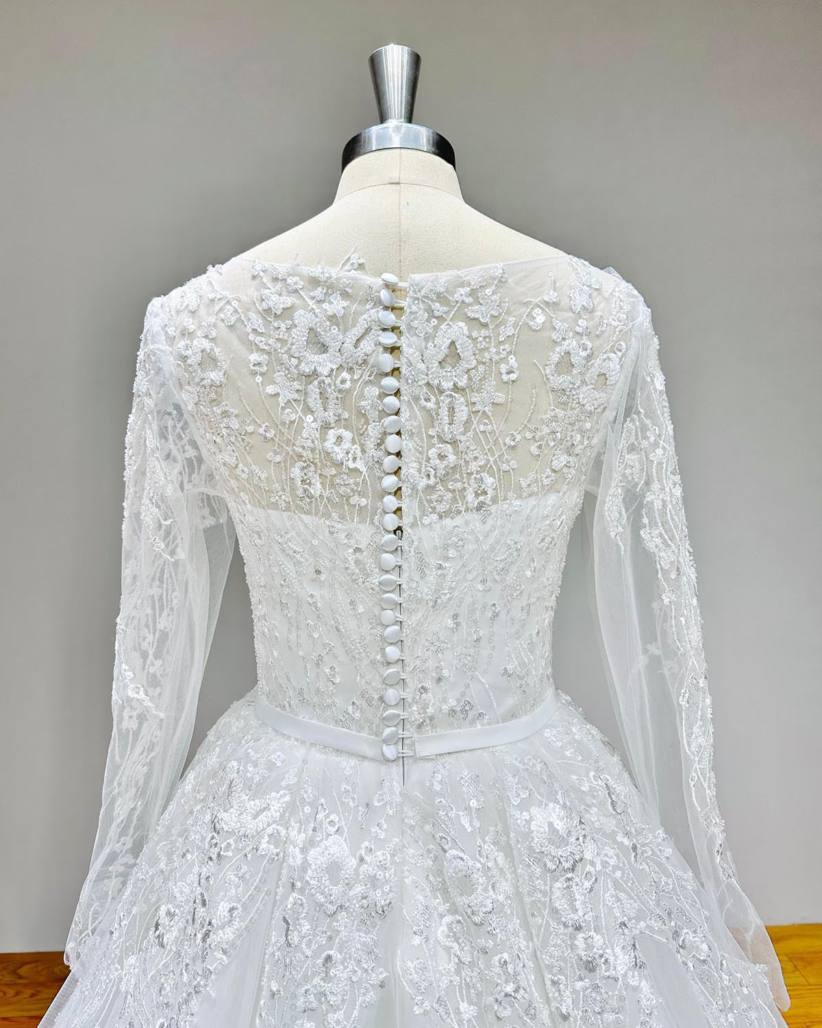 Back detail of a long-sleeve tulle wedding dress featuring elegant button-up closure and floral lace appliqué.