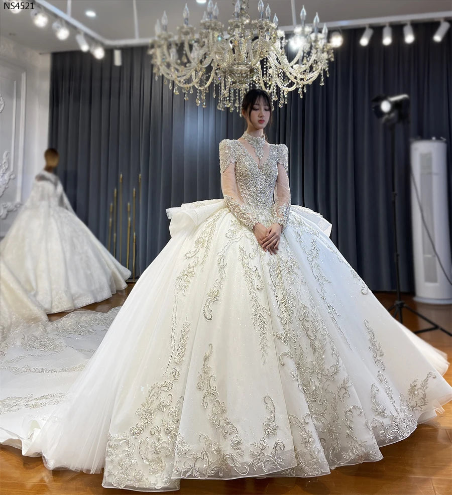 Elegant front-side view of a luxury V-neck ball gown wedding dress featuring long sleeves, heavy crystal beadwork, and a voluminous shimmering skirt on a model.