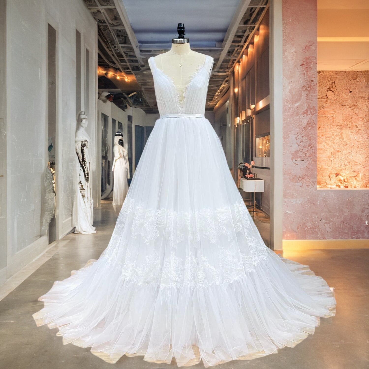 White sleeveless beach bridal dress with a structured pleated mesh bodice and a lightweight flared tulle skirt, shown on a mannequin in a bridal shop corridor.