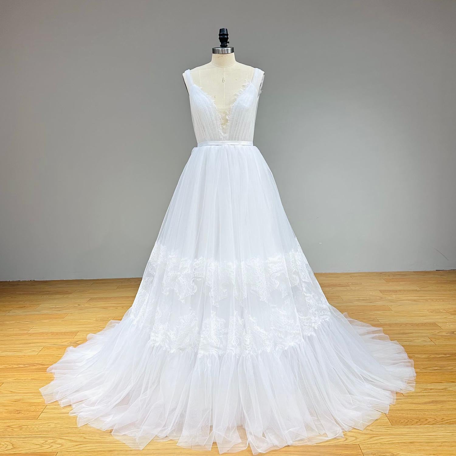 Studio front portrait of a minimalist white tulle wedding gown on a mannequin, showcasing a satin waistband and a soft tiered lace panel design on the skirt.