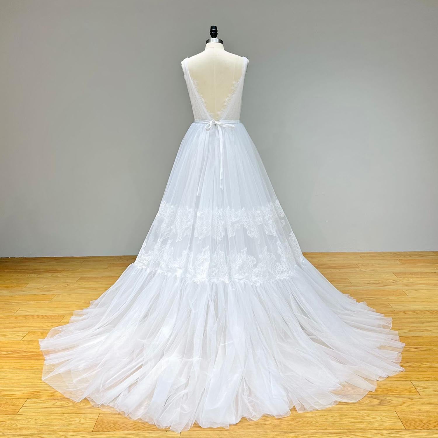 Studio back view of a low backless beach wedding dress on a mannequin, highlighting the deep V-back cutout design, delicate lace trim, and a dainty satin ribbon tie at the waist.