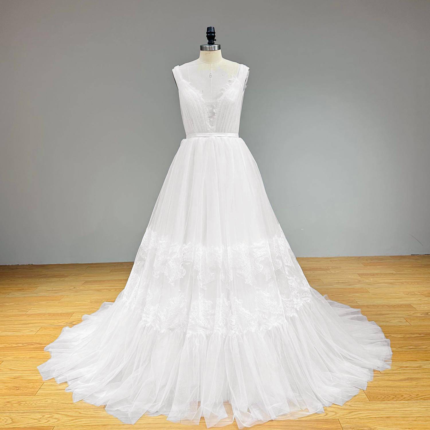 Full-length front perspective of the simple bohemian tulle-and-lace wedding dress on a dress form against a neutral gray background.