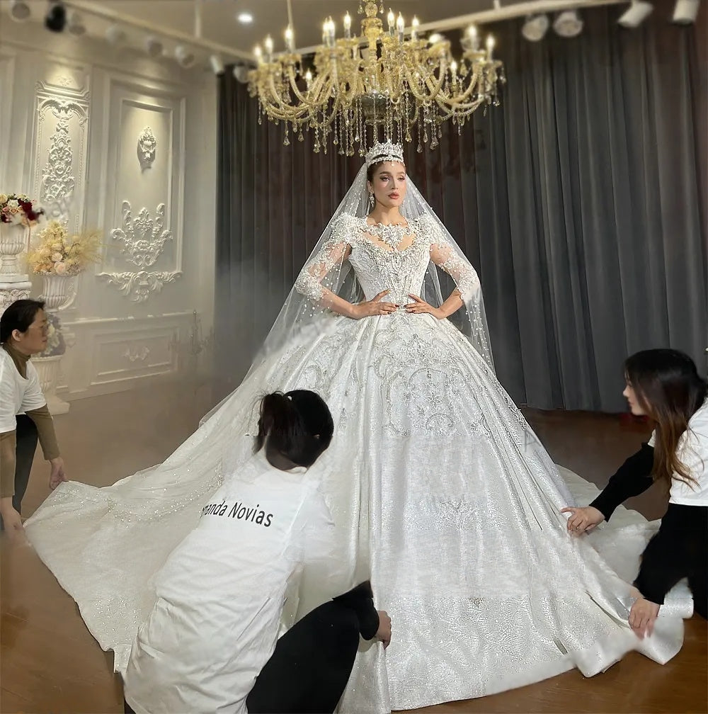 Professional mannequin display of an empire lace appliquéd bridal gown with intricate crystal embellishments, long sleeves, and a voluminous sparkling skirt.