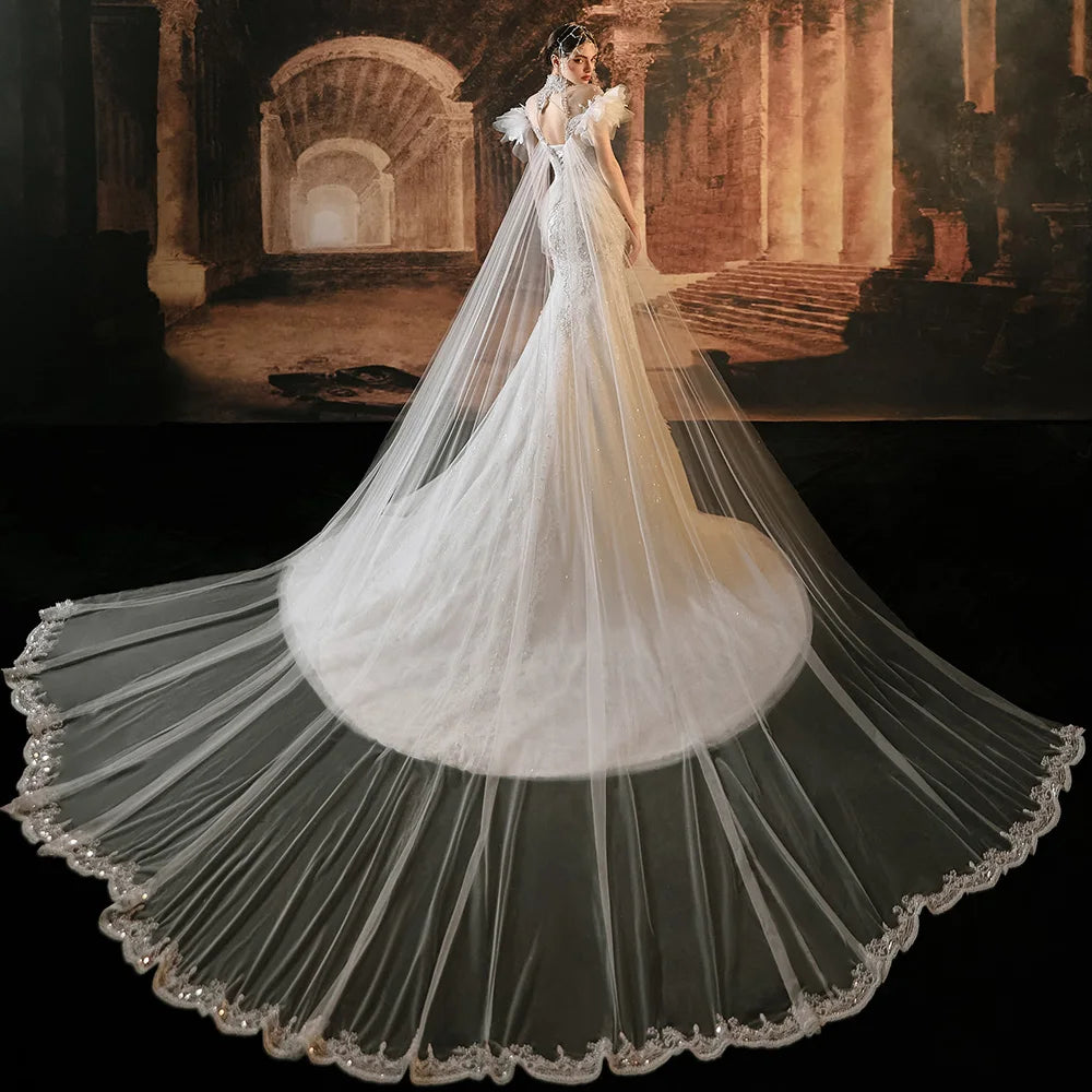 Breathtaking rear view of a luxury mermaid bridal gown highlighting a massive, sheer tulle Watteau train with an intricate lace-trimmed border and an elegant open-back design.