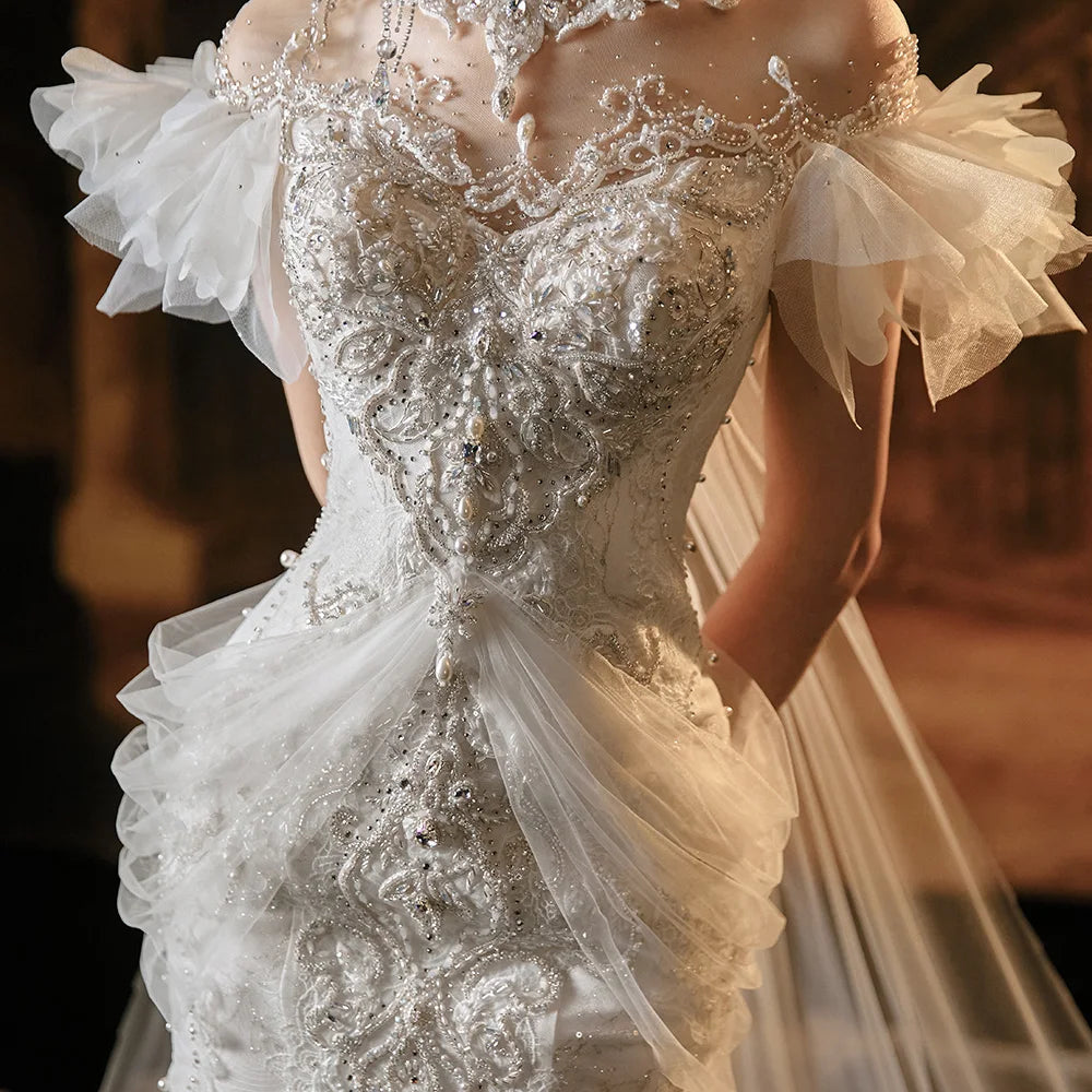 Close-up detail of a bridal bodice featuring handcrafted silver beadwork, ornate lace patterns, and delicate draped tulle accents on a luxury high-neck mermaid wedding gown.