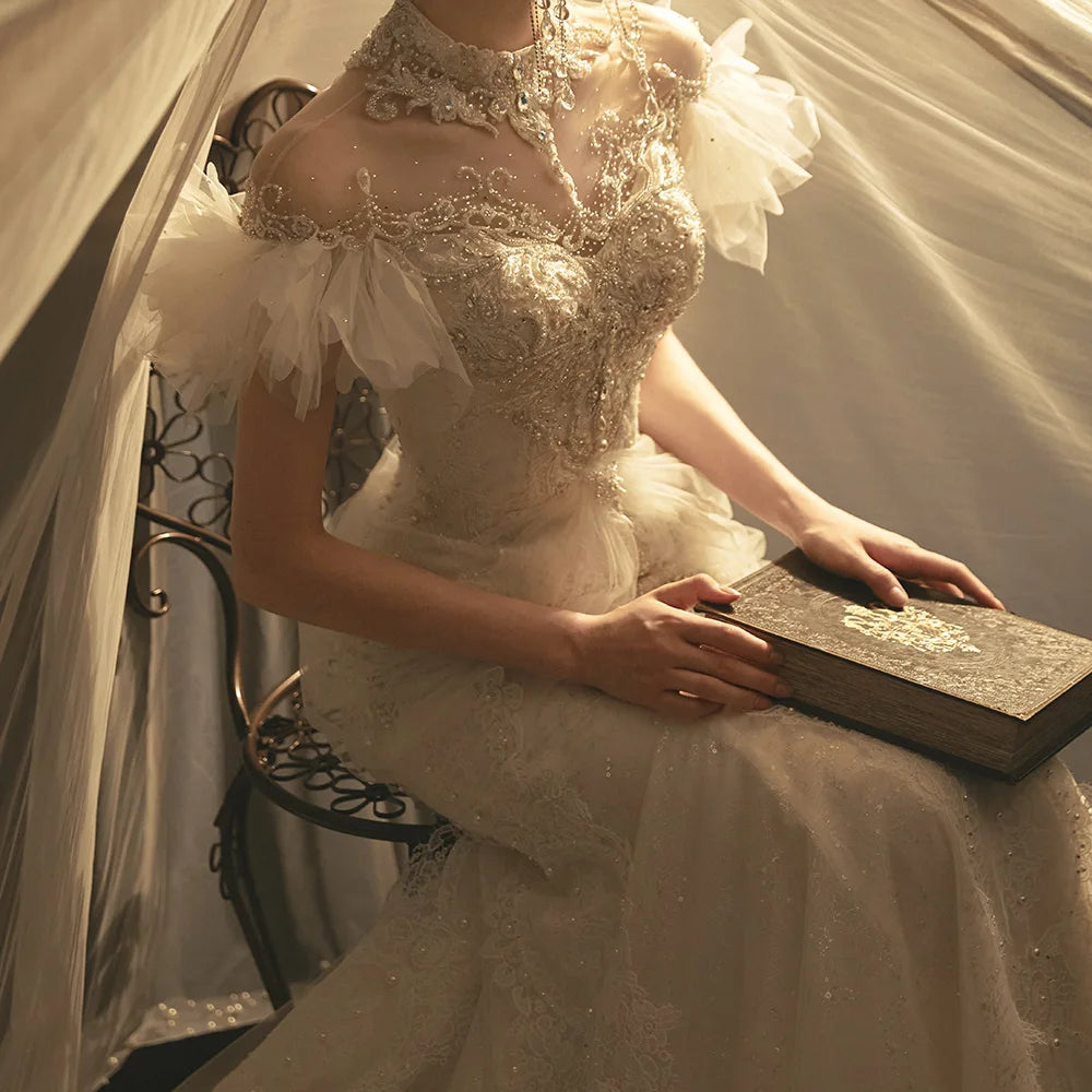 Sophisticated upper body view of a luxury wedding dress emphasizing the illusion high neck adorned with jewels, intricate floral lace appliqués, and romantic flutter sleeves.