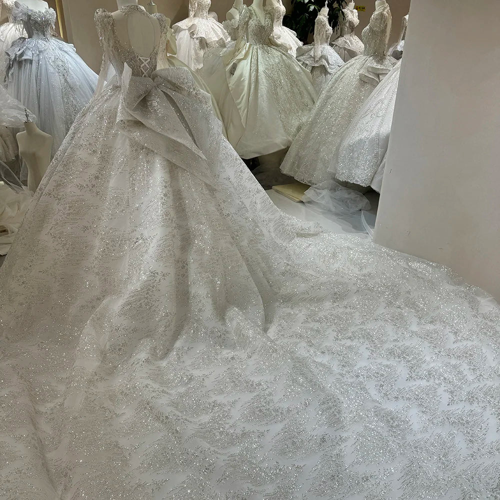 Close back view of a sequined wedding dress on a mannequin, showcasing the keyhole cut-out back, lace-up corset closure, giant decorative bow, and a sprawling chapel train.