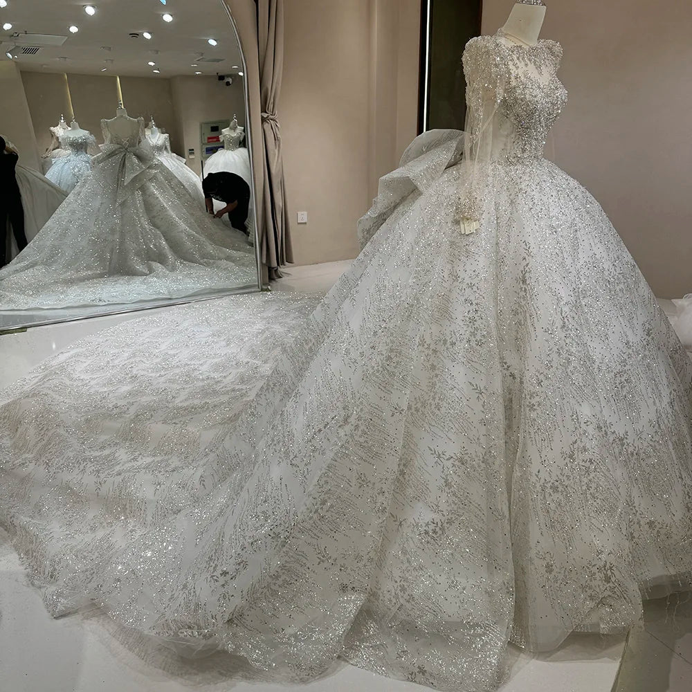 Side profile view of a glittering white tulle ball gown wedding dress on a mannequin, emphasizing the grand volume of the skirt and the length of the heavily sequined train.
